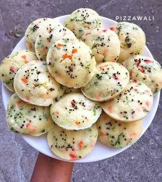 a person holding a white plate filled with small cookies covered in sprinkles