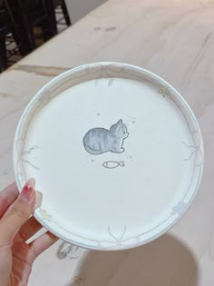 a hand holding a white plate with a cat on the front and bottom part of it