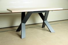 a wooden table sitting on top of a tiled floor next to a white wall with black metal legs