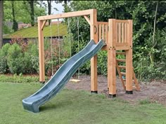 a wooden swing set with a slide and climbing frame in the back yard, surrounded by trees