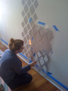 a woman sitting on the floor painting a wall with blue tape and paint rollers