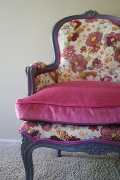 an old chair with pink and purple fabric on it's back, in front of a white wall