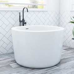 a white bath tub sitting on top of a tiled floor next to a window and potted plant