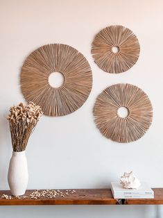 three circular wicker wall hangings on a white wall above a wooden table with dried flowers