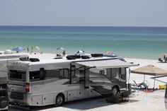 an rv parked on the beach next to some umbrellas