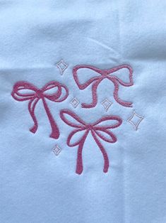 two bows are embroidered onto the back of a white t - shirt with pink thread