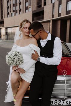 a bride and groom sitting on the back of a car in front of a building