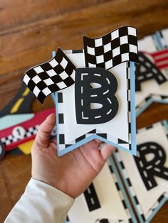 a person holding up a card with the letter b on it and checkered ribbon