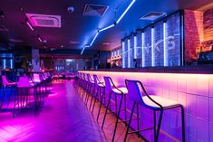 the bar is lit up with purple lights and blue barstools in front of it