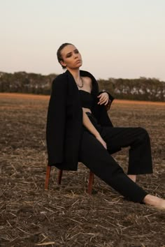 a woman is sitting on a chair in the middle of a field with her legs crossed