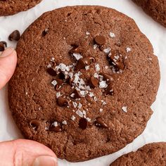 a close up of a person touching a chocolate cookie with sea salt on top and other cookies in the background