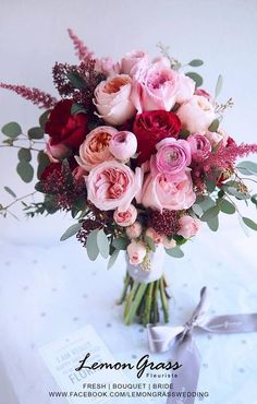 a bouquet of pink and red flowers sitting on top of a white table with silver ribbon