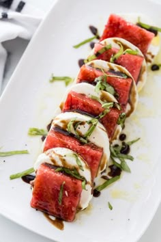 slices of watermelon and black olives on a white platter with sauce