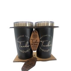 two black tumblers sitting on top of a cardboard box next to a wooden spoon