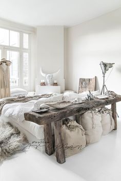 a bed with pillows and blankets on top of it next to a wooden bench in front of a window