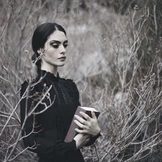 a woman is standing in the woods holding a book and looking off into the distance