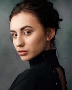 a young woman is posing for the camera with her hair in a high bun and wearing a black turtle neck sweater