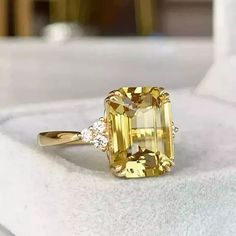 a fancy yellow diamond ring sitting on top of a white surface with diamonds around it