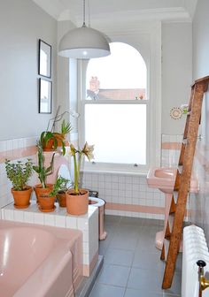 a bathroom with pink tiles and potted plants on the window sill, next to a ladder