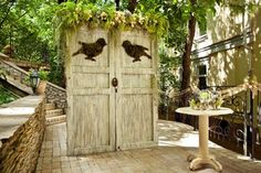 two wooden doors with birds on them in the middle of a patio surrounded by trees