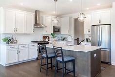 a large kitchen with white cabinets and stainless steel appliances, along with two blue bar stools