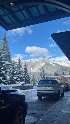 cars parked on the side of a road in front of snow covered mountains and pine trees