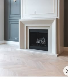 an empty fireplace in the middle of a room with wood flooring and gray cabinets