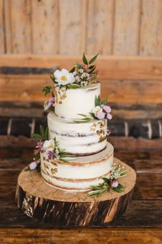 a three tiered wedding cake with flowers on top sits on a piece of wood