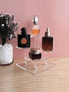 three different perfume bottles sitting on top of a clear shelf next to a vase with flowers