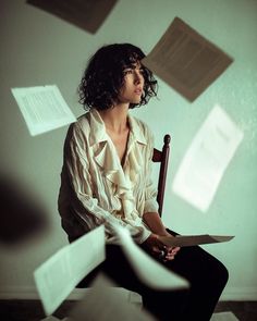 a woman sitting in a chair with papers flying around her