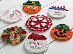 six crocheted christmas ornaments are arranged on a white wooden surface, each with different faces