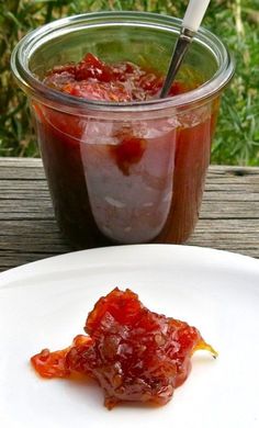 a jar of jelly with a spoon in it sitting on a table next to a white plate