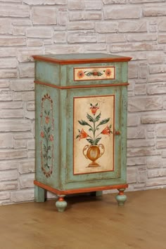 an old painted cabinet sitting in front of a brick wall with a vase on it