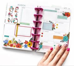 a woman's hand is holding an open planner book with flowers on the pages