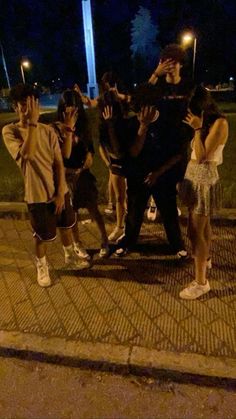 a group of people standing on the side of a road at night with their arms in the air