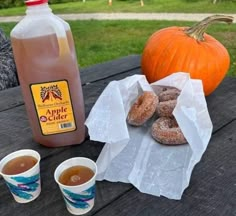 doughnuts, coffee and apple cider are on a picnic table with pumpkins in the background