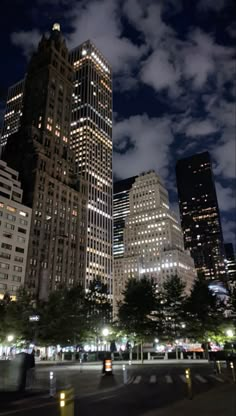 the city is lit up at night with clouds in the sky and people walking on the sidewalk