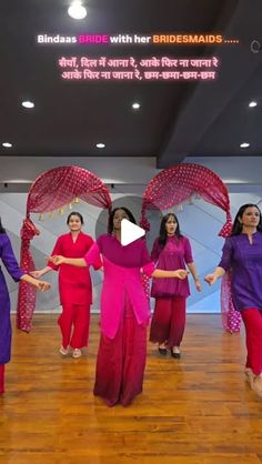 a group of women in purple and pink outfits dancing on a wooden floor with red umbrellas