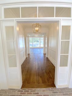 an empty room with white walls and wooden floors, open doors leading to another room