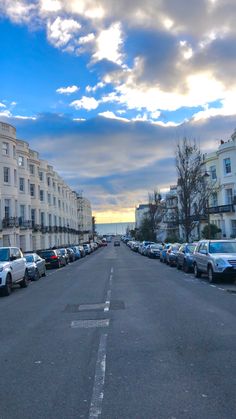 cars are parked on the side of an empty street in front of apartment buildings at sunset