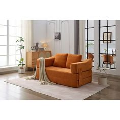 an orange couch sitting on top of a rug in a living room next to a window