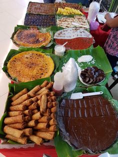 many different types of desserts are on display at a buffet table with banana leaves