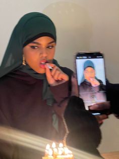 a woman brushing her teeth in front of a birthday cake with candles on it and a cell phone