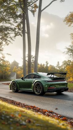 a green sports car driving down a road next to some trees and leaves on the ground