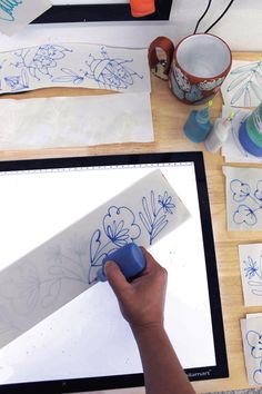 someone is drawing flowers on paper with blue marker and pen while using a tablet computer