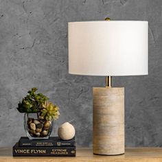 a table with a lamp and some books on it next to a plant in a vase