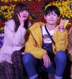 three people sitting next to each other in front of flowers and one person making the peace sign