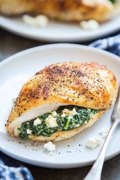 a white plate topped with a cut in half chicken and spinach covered in cheese