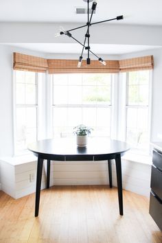 a dining room table with a potted plant on it in front of two windows