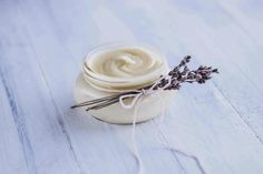 a jar filled with cream sitting on top of a white wooden table next to a sprig of lavender